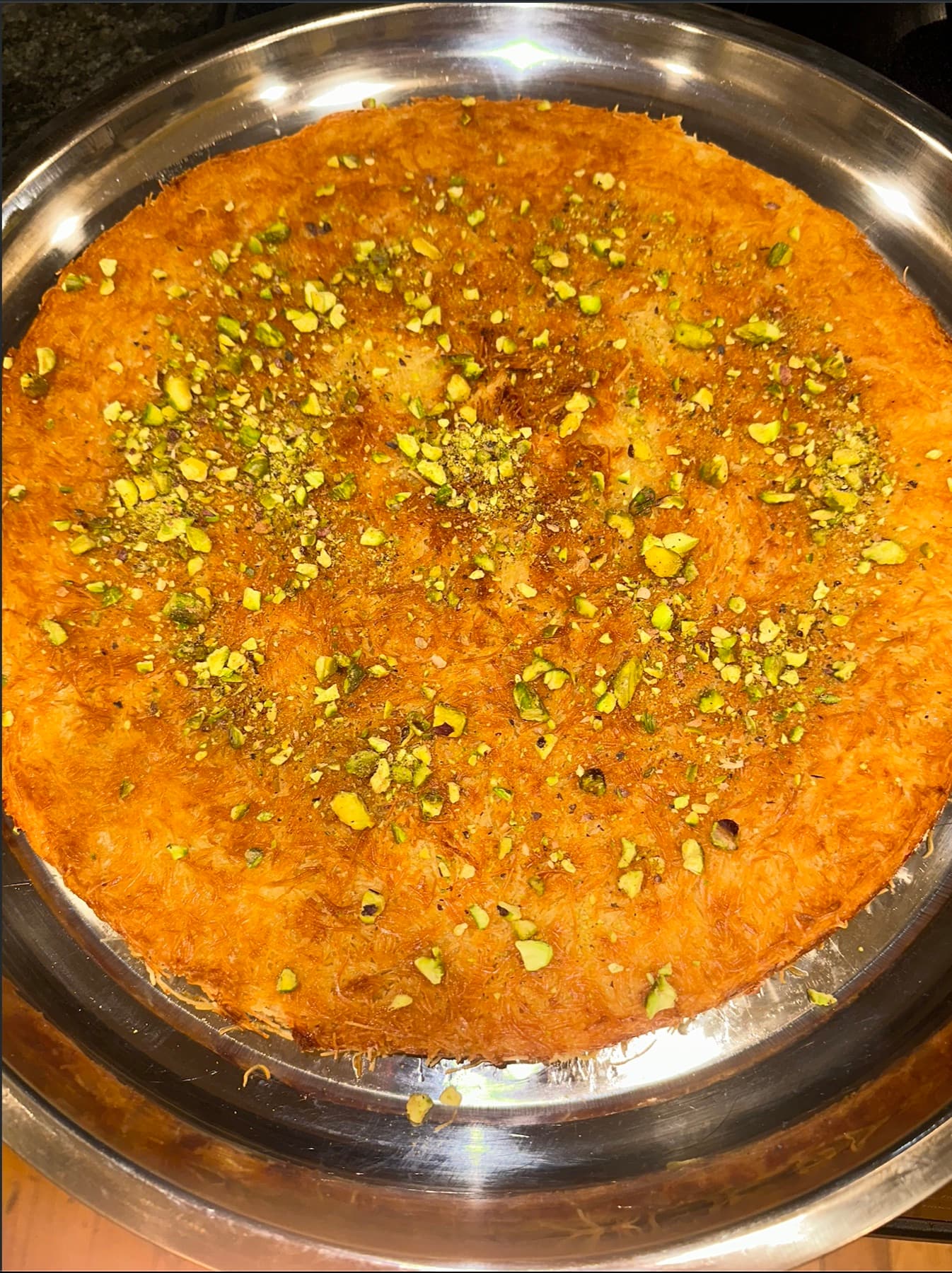A whole round tray of golden Palestinian knafe topped with crushed pistachios, fresh from the oven